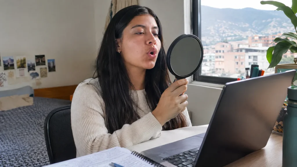 Woman practicing sounds with a hand mirror at her desk - Mouth Training for Sounds: What It Is and How Inpronunci Uses It